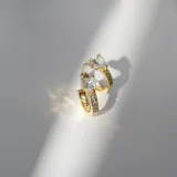 Par de aros dorados con forma de argolla con bisagra, mini cristales y cristal en forma de corazón engarzada. Fabricados en acero con baño en oro de 18k.