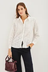 Camisa de manga larga en color blanco, confeccionada en tejido de algodón con diseño calado tipo broderie. Presenta cuello clásico, cierre frontal con botones y paneles frontales con tablas verticales.