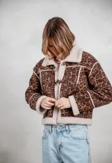 Campera de gamuza con estampado animal print de leopardo, forrada en corderito sintético color crema. Presenta cierre frontal con botones tipo toggle, cuello solapa y detalles de costuras visibles.