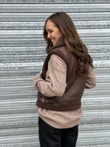 Chaleco gamulán corto marrón de efecto cuero, con interior y detalles de corderito sintético a tono. Cuenta con cuello alto y tiras laterales con hebilla para ajustar la cintura.