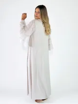 Vestido largo negro de corte holgado, con escote en V y mangas largas con volados en los puños.