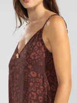 Vestido largo de corte fluido con escote en V profundo y finos breteles. Presenta un estampado animal print combinado con rayas y un detalle decorativo de flor en cobre en el centro del escote.