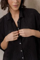 Camisola blanca de silueta amplia y caída liviana, con diseño clásico de cuello camisero, cierre frontal con botones y mangas tres cuartos, decorada con grandes motivos florales bordados.