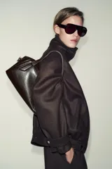 Bolso de mano y bandolera color marrón oscuro, con forma redondeada y doble asa superior. Presenta cierre principal de cremallera y un bolsillo interior con cierre.