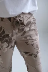 Pantalón de corte recto y ajuste holgado, color visón con estampado floral en tonos tierra. Presenta cintura elástica con cordón ajustable y ruedos doblados.