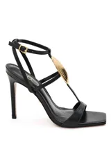 Sandalias de tacón alto PatBo modelo Zulu, color dorado metalizado, con tira en la puntera, diseño en T con aplique rígido en forma de concha marina, correa ajustable al tobillo y plantilla marrón.