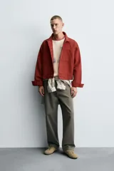 Cazadora de algodón color terracota, de corte cropped y calce holgado. Presenta cuello solapa, manga larga con puño abotonado, dos bolsillos de vivo en el pecho y bolsillos laterales en la cadera. Cierre frontal con botonadura oculta.