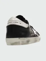 Zapatillas Golden Goose modelo Super-Star, color negro con estrella plateada y detalles en cuero blanco en el talón.