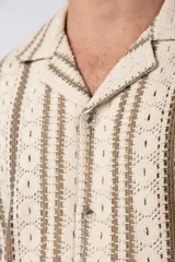 Camisa de manga corta tejida al crochet con diseño de rayas verticales negras sobre una base color crudo. Presenta cuello solapa y cierre frontal con botones.