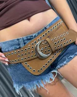 Cinturón ancho de gamuza color tostado con múltiples filas de ojalillos metálicos plateados y hebilla grande en forma de media luna.