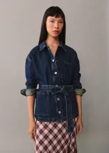Chaqueta vaquera azul con cuello camisero, cierre frontal con botones metálicos, tres bolsillos delanteros, mangas largas con puños abotonados y cinturón de lazo.