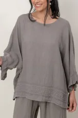 Blusa de lino color verde militar, holgada, de manga 3/4 con volados en los puños, cuello redondo y detalle de alforzas horizontales en el dobladillo.