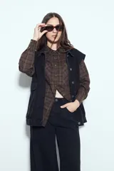 Camisa tipo leñadora de corte oversize, con estampado de cuadros en tonos negro y marrón. Presenta cuello clásico, cierre frontal con botones y mangas largas con puños abotonados.