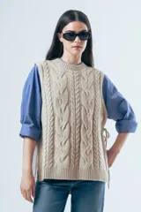 Chaleco de punto color marrón con diseño de ochos, cuello redondo y lazos laterales ajustables.