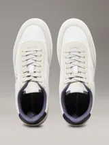 Zapatillas de corte bajo Calvin Klein, con diseño minimalista en color blanco y beige. Presentan una combinación de materiales en la capellada, incluyendo piel y ante, con detalles en contraste en el talón y logo de la marca en el lateral y la mediasuela.