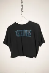 Remera negra de corte cropped con estampa frontal en color turquesa con la palabra Weltschmerz.