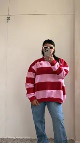Buzo oversize a rayas horizontales rosas y rojas con cuello redondo y logo bordado en el pecho.
