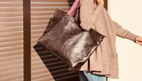 Bolso XL de cuero color marrón oscuro, con asas cortas de cuero y correa larga de tela estampada a rayas rojas y blancas.