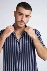 Camisa de manga corta con diseño a rayas verticales en color azul marino y blanco. Presenta cuello clásico, cartera abotonada frontal y logo bordado en el pecho. Posee un corte slim fit.