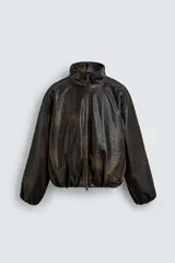Cazadora de corte relajado confeccionada en tejido efecto piel con acabado lavado. Presenta cuello subido, cierre frontal de cremallera, mangas largas con puños elásticos y ruedo elástico. Incluye bolsillos laterales y un bolsillo interior.