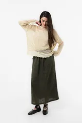 Sweater beige de punto abierto y liviano, con escote redondo, mangas largas, silueta amplia y detalle de broderie en el ruedo.