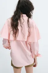 Camisa rosada de cuello solapa y manga larga, con detalle de volantes en las sisas y cierre frontal oculto con botones.