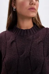 Sweater de punto con diseño de trenzas verticales, cuello redondo y mangas largas. Presenta un corte holgado y terminaciones acanaladas en cuello, puños y ruedo.