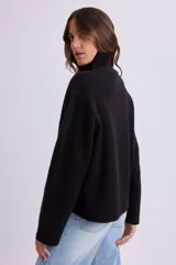 Buzo de punto en color negro, con cuello alto y puños y ruedo acanalados. Presenta un diseño de corte recto y tejido elástico.
