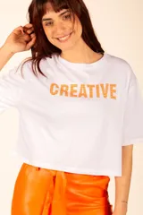Remera blanca de corte crop con mangas cortas y estampado de la palabra "CREATIVE" en color naranja.