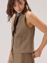 Chaleco negro sin mangas, de corte recto y largo a la cintura, con cuello redondo y cierre frontal oculto.