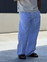 Pantalón de corte ancho y holgado, con diseño de rayas verticales finas en color azul y blanco. Presenta cintura elástica con cordón ajustable y un pequeño bordado en color rojo en la parte superior.