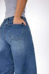 Pantalón de jean con corte balloon fit, de tiro alto y diseño holgado en las piernas. Confeccionado en denim con elastano, presenta un lavado azul clásico y cierre frontal con botón y cremallera.