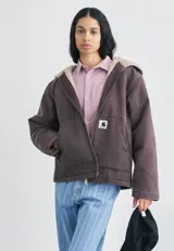 Campera con capucha Carhartt WIP modelo Mitch, color marrón oscuro, confeccionada en lona de algodón de peso medio con forro interno de corderito sintético. Cuenta con cierre frontal bidireccional, bolsillos frontales tipo parche y etiqueta cuadrada tejida con el logo de la marca.