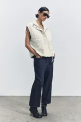 Chaleco gris acolchado con cuello alto, cierre frontal con cremallera metálica, bolsillos de plastrón en delantero y bajo ajustable con cordones.