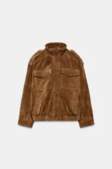 Cazadora de piel de ante 100% color marrón, con cuello subido, manga larga y bolsillos frontales con solapa. Presenta bajo elástico y cierre frontal con cremallera y botones a presión ocultos.