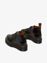 Botas Dr. Martens modelo Church Quad de cuero negro, con plataforma gruesa acanalada, costuras amarillas contrastantes y cordones negros.