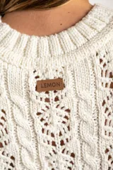 Top sin mangas de tejido de punto calado, color blanco, con cuello redondo acanalado y diseño de trenzas verticales. Presenta un ruedo con terminación festoneada.