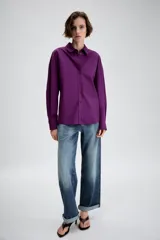 Camisa de manga larga en color violeta, con cuello solapa y cierre frontal de botones. Presenta un diseño de corte recto con detalle de pliegues en la espalda.