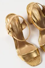 Sandalias de tacón alto color lila, con tira delantera y tobillera con hebilla dorada.