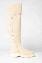 Bota bucanera de gamuza color crema, con caña alta y detalle de tachas plateadas.
