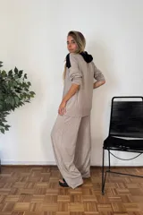 Sudadera tipo canguro con capucha y cordones, de manga larga y corte amplio. Presenta un diseño bicolor: la parte superior (hombros y capucha) es negra, y el resto del cuerpo y mangas son de color beige oscuro/topo.