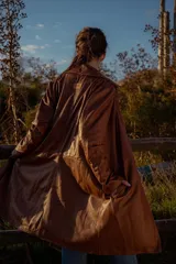 Gabardina marrón de cuero ovino italiano, con cuello camisero, cierre frontal con botones, mangas largas y corte recto.