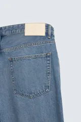 Pantalón de jean con corte recto desde la cadera hasta el tobillo, de tiro medio y ajuste holgado. Presenta diseño de cinco bolsillos, cierre frontal con cremallera y botón, y acabado con efecto lavado.