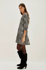 Vestido corto de algodón con estampado tipo mosaico en tonos blanco, negro y gris. Presenta escote en V profundo, mangas tres cuartos y falda con volado en el ruedo.