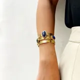 Brazalete tipo puño de bronce con acabado martillado y tres piedras engarzadas de forma ovalada, rombo y circular.