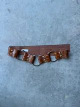 Cinturón marrón con textura símil piel de cocodrilo, argollas plateadas y remaches.