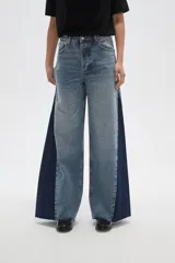 Pantalon de jean de corte ancho con diseño color block, combinando paneles de denim lavado claro en el centro y denim azul oscuro en los laterales. Presenta tiro medio y terminaciones deshilachadas en el ruedo.