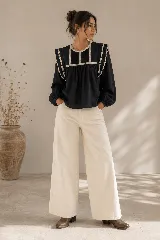 Blusa color tostado con cuello redondo, mangas largas abullonadas con puños elastizados, y detalles de puntillas y bordados en el frente y hombros.
