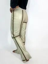 Pantalón de cuero color crema con apliques de cintas marrones. De tiro medio alto, sin bolsillos y corte acampanado.