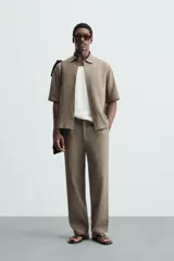 Pantalón de calce relajado confeccionado en tejido de viscosa y yute color tostado. Presenta cintura elástica ajustable con cordón, bolsillos laterales, bolsillos traseros de vivo y cierre frontal con cremallera y botón.